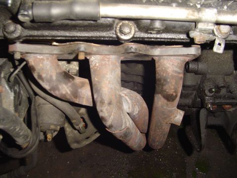 1994 Ford Probe - Close-up view of a rusty exhaust manifold with visible bolts and hoses.