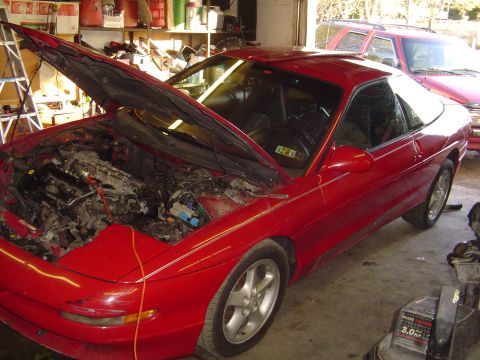 1994 Ford Probe - A red 1994 Ford Probe is shown with its hood open, revealing the engine bay, in what appears to be a garage setting.