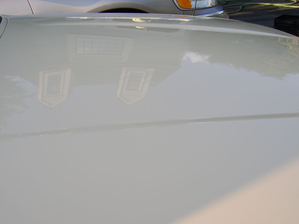 Glossy silver car panel reflecting a house and trees