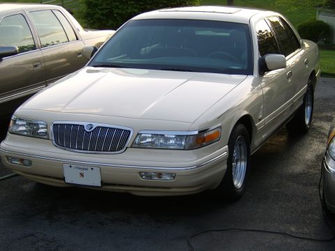 1996 Mercury Grand Marquis - A cream-colored sedan with a prominent chrome grille is parked outdoors next to another vehicle.