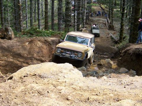 1968 Ford Bronco - A 1968 Ford Bronco tackles a challenging off-road course with other vehicles and spectators in the background.