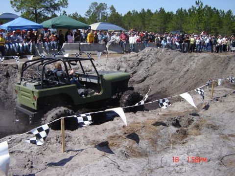 1989 Ford Bronco - A Jeep tackles a challenging off-road course during an event, with a crowd gathered to watch the action.