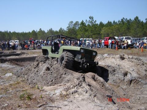 1989 Ford Bronco - A crowd watches as a modified Jeep navigates a challenging dirt obstacle during an outdoor event.