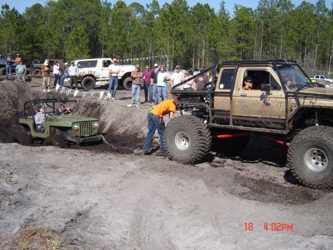 1989 Ford Bronco - Off-road vehicles navigate a muddy course with onlookers present.