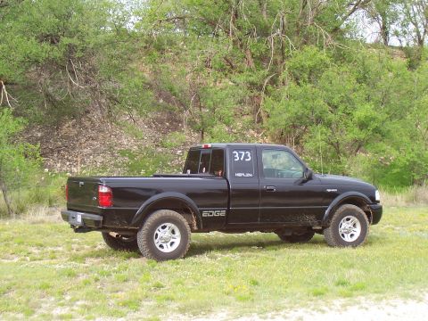 2003 Ford Ranger - This black 2003 Ford Ranger Edge pickup truck is seen from a 3/4 front angle, parked in a grassy area with trees in the background.