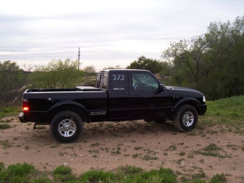 2003 Ford Ranger - A black 2003 Ford Ranger Edge pickup truck is parked on a dirt road with trees and brush in the background.