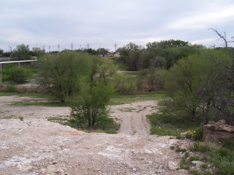2003 Ford Ranger - A dirt road winds through a dry creek bed surrounded by vegetation under an overcast sky.