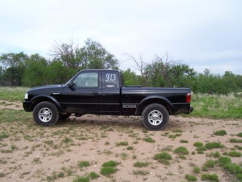 2003 Ford Ranger - A black Ford Ranger pickup truck is parked on a dirt lot with sparse vegetation and trees in the background.