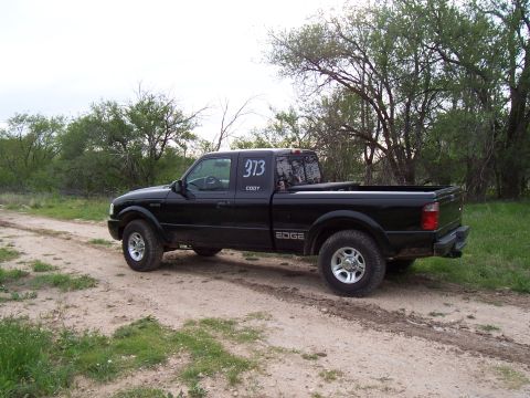 2003 Ford Ranger - A black 2003 Ford Ranger Edge pickup truck is parked on a dirt road with trees in the background. The truck has the number 373 and the name…