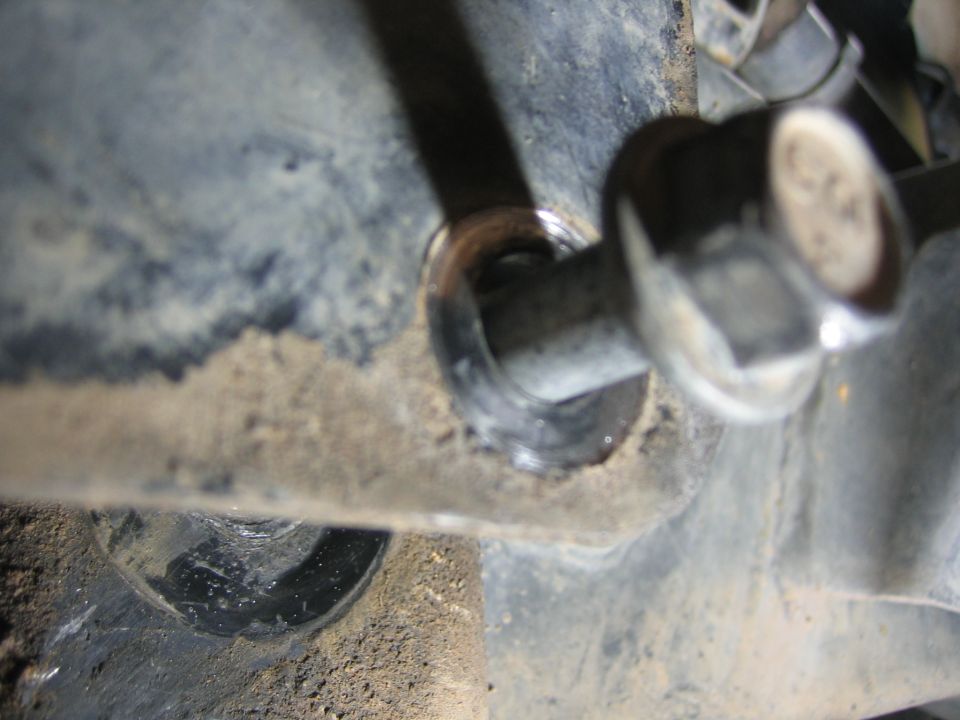 Close-up of a bolt passing through a metal bracket on a dirty vehicle suspension component