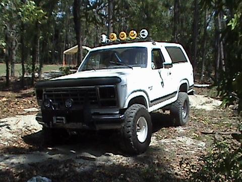 1986 Ford Bronco - 1986 Ford Bronco modified for off-road use, parked in a wooded area.