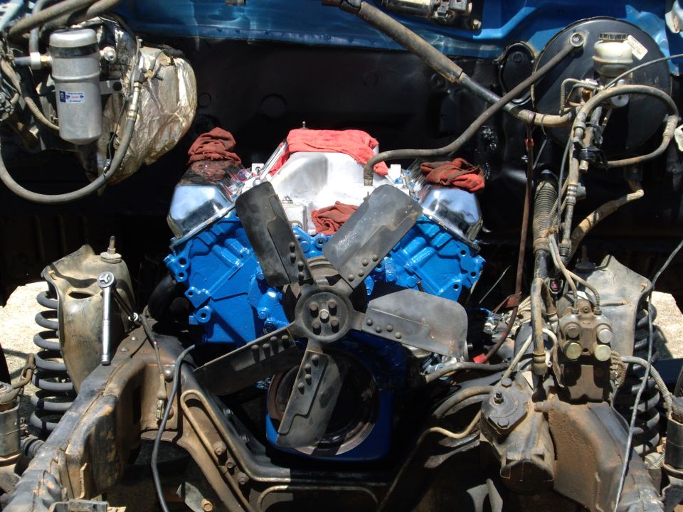 Engine bay with a blue V8 engine, fan, and various hoses and components. Some red cloths are placed on top of the engine
