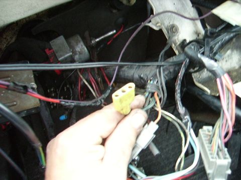 1978 Ford Bronco - Close-up of a vehicle's interior wiring harness with a hand holding a connector.