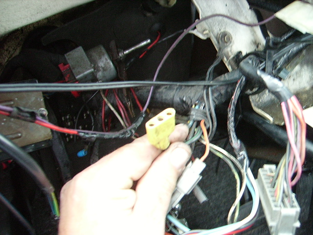 Hand holding a yellow electrical connector with multiple wires connected to a vehicle's wiring harness