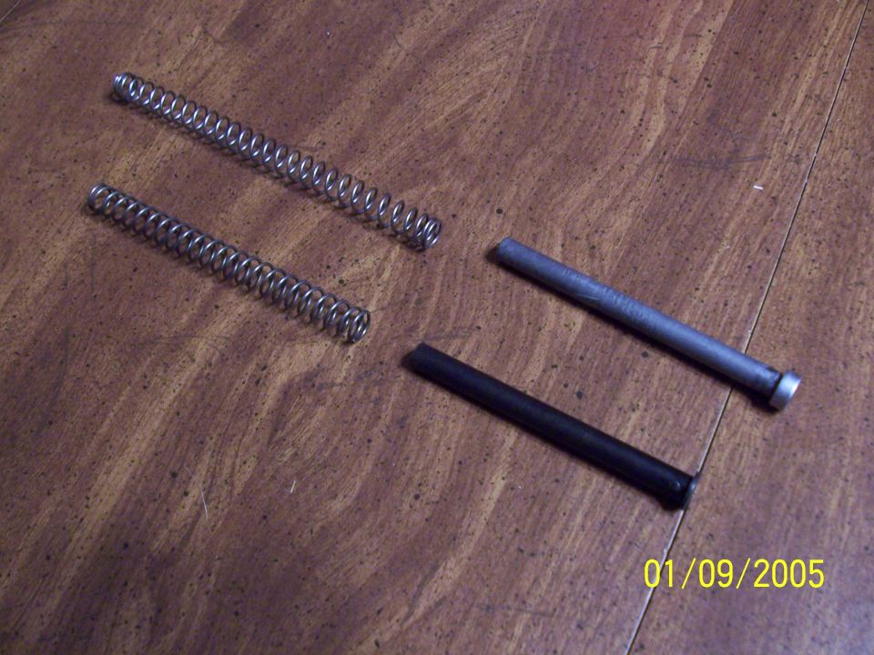 Two coil springs and two pins laid out on a wood table, dated 01/09/2005
