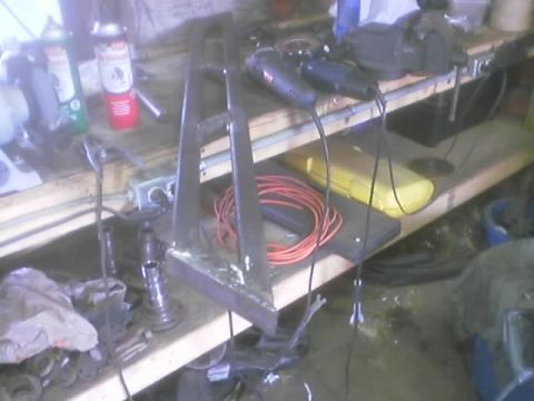 1989 Ford Bronco - A metal bracket sits on a workbench with tools and supplies, suggesting a fabrication project.