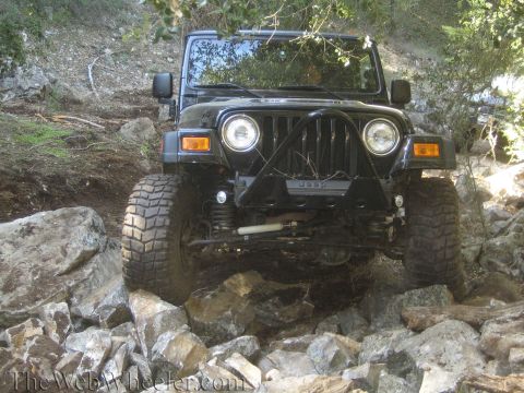 1987 Suzuki Samurai - A black Jeep Wrangler navigates a challenging rocky path off-road.