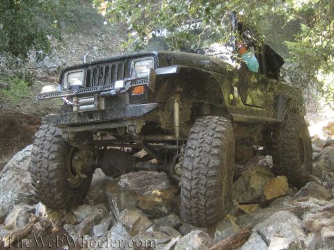1987 Suzuki Samurai - This black Jeep Wrangler is shown tackling a challenging rocky trail, demonstrating its off-road capabilities.