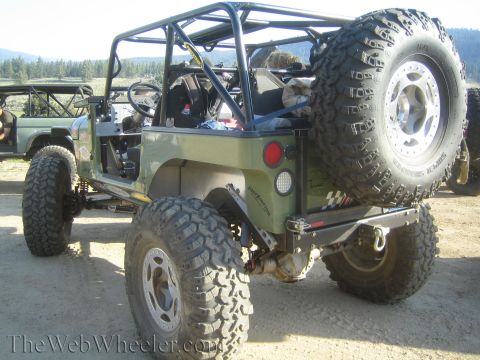 1987 Suzuki Samurai - An olive green off-road vehicle with a roll cage is parked on a dirt road next to another vehicle.