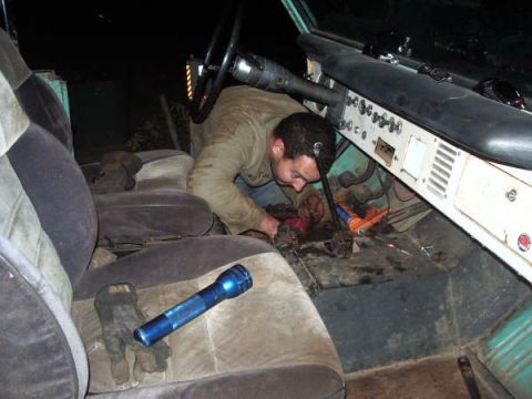 1968 Ford Bronco - A person is working on the floor of a vehicle's interior, with tools and a flashlight nearby.