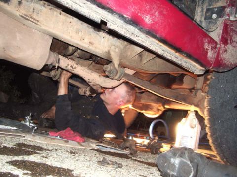 1968 Ford Bronco - A mechanic works on the underside of a red vehicle, focusing on the exhaust system and suspension components.
