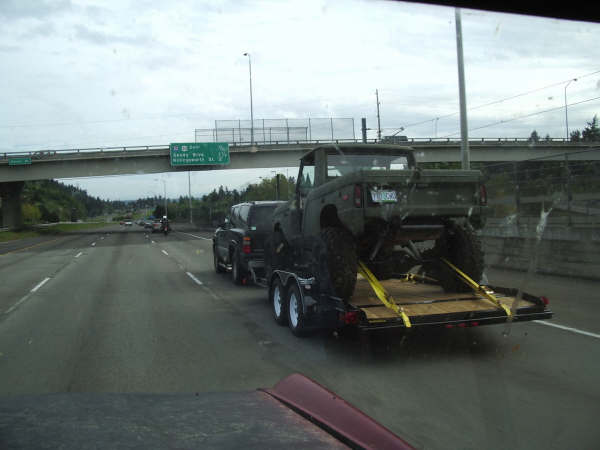 Olive green pickup truck on trailer, rear view. License plate visible