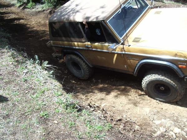 Gold 1968 Ford Bronco driving on a dirt trail with trees around