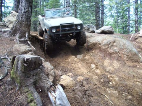 1968 Ford Bronco - A 1968 Ford Bronco navigates a challenging rocky terrain in a wooded area.