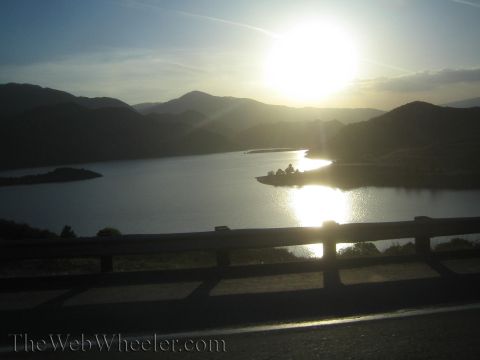 1987 Suzuki Samurai - A lake and mountain landscape is captured during a vibrant sunset, with the sun's reflection shimmering on the water's surface.