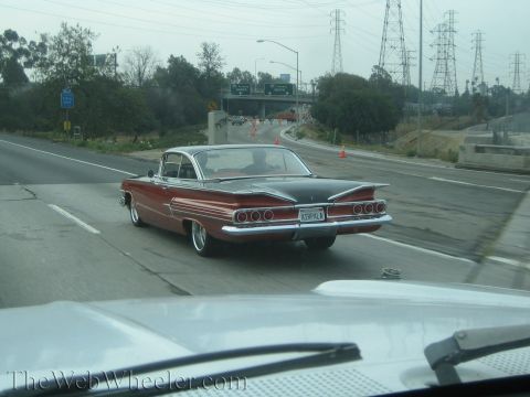 1990 Ford Bronco - red and white finned classic Chevrolet drives down a multi-lane highway, photographed from a following vehicle.