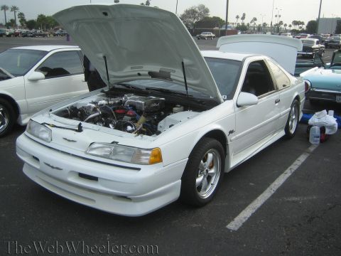 1990 Ford Bronco - white Ford Thunderbird Super Coupe with its hood up showing the engine, parked at an outdoor car show.