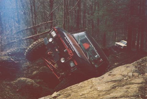 1978 Ford Bronco - Off-road vehicles tackle a challenging, rocky terrain in a wooded area.