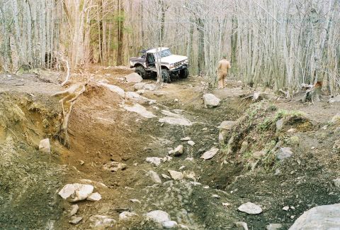 1978 Ford Bronco - A person walks away from an off-road vehicle on a challenging, rocky path through a forest.