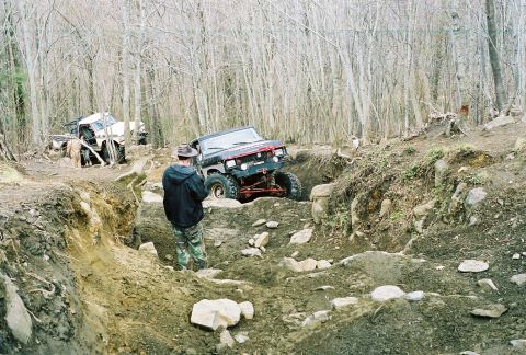 1978 Ford Bronco - Off-road vehicles tackle a challenging, muddy, and rocky terrain in a wooded environment.