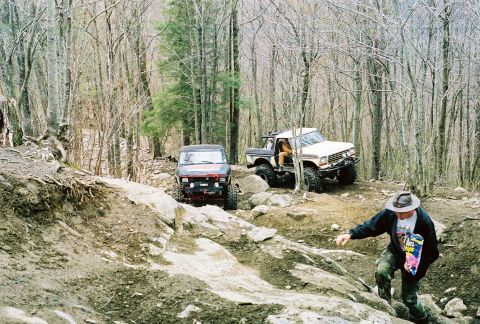 1978 Ford Bronco - Two off-road vehicles navigate a challenging rocky path through a dense forest.