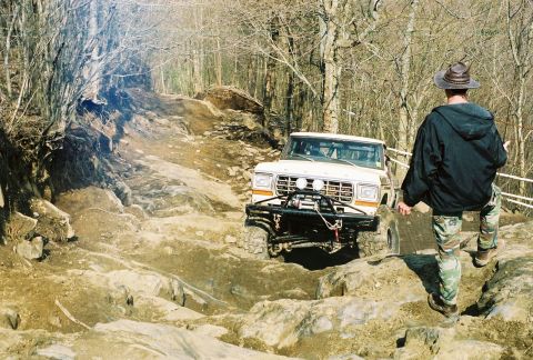 1978 Ford Bronco - A white 1978 Ford Bronco navigates a challenging rocky trail with a person walking nearby.
