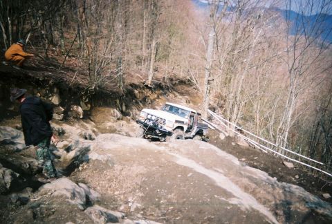 1978 Ford Bronco - An off-road vehicle attempts to climb a challenging, rocky incline with assistance from onlookers.