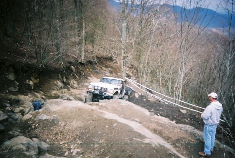 1978 Ford Bronco - A white 1978 Ford Bronco tackles a challenging off-road course on a wooded mountainside.