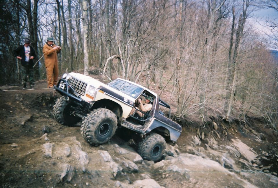 Modified 1978 Ford Bronco climbing a steep, rocky trail with two people watching