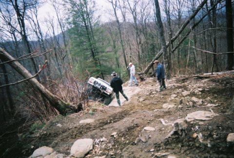 1978 Ford Bronco - Off-road vehicle stuck on a steep, wooded trail with onlookers.