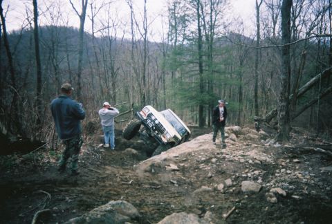 1978 Ford Bronco - A white off-road SUV navigates a challenging rocky incline in a wooded area.
