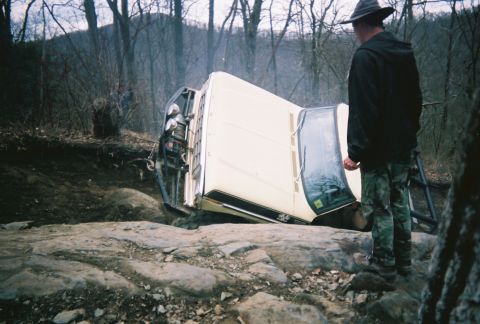 1978 Ford Bronco - A white 1978 Ford Bronco is tipped on its side on a , rocky trail in a wooded area.