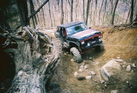 1978 Ford Bronco - Off-road vehicle navigates a challenging dirt trail with a large fallen tree on the left.