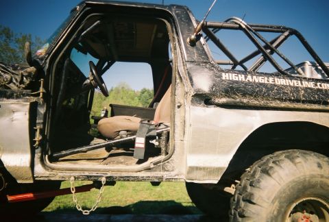 1978 Ford Bronco - Mud-splattered off-road truck with roll cage and open driver's door, showing interior.