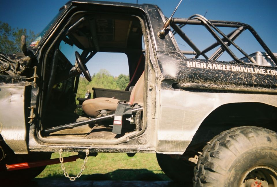 Mud-splattered off-road truck with roll cage and open driver's door, showing interior