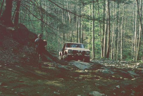 1978 Ford Bronco - An off-road vehicle navigates a trail surrounded by dense foliage.