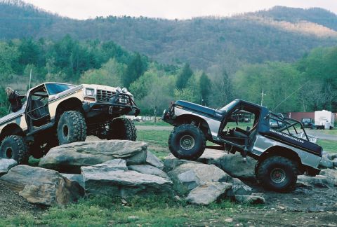 1978 Ford Bronco - Two off-road vehicles navigate a rocky terrain, with a mountainous landscape in the background.