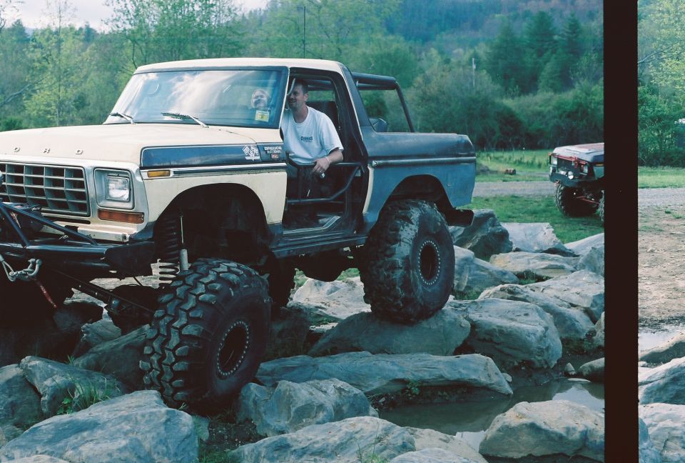 Tan and blue 1978 Ford Bronco with large off-road tires navigating rocks