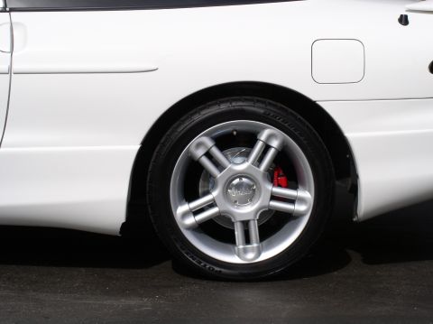 1996 Ford Probe - Side close-up of the rear wheel on a white coupe, showing a silver five-spoke alloy wheel with a low-profile tire and a red-painted brake c…