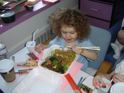 1993 Ford Bronco - A young child with curly hair eats a meal of noodles and beef with broccoli from a takeout container using chopsticks.